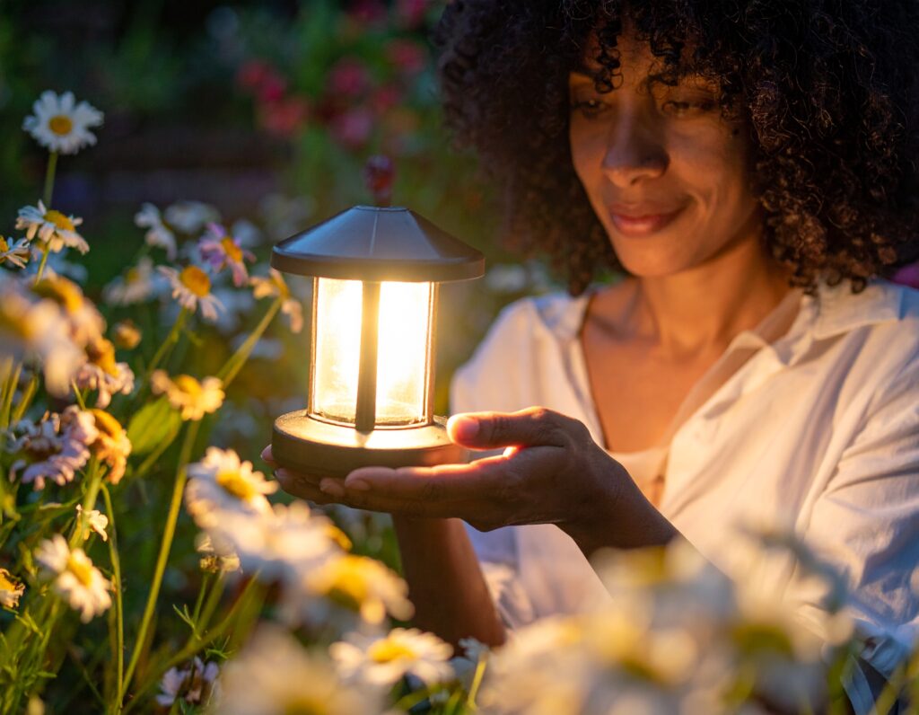 Femme cherchant comment activer une lampe solaire de jardin au milieu de quelque fleurs